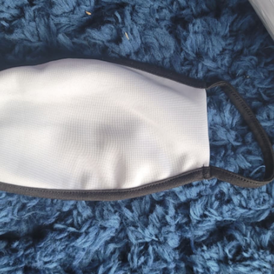 A white face mask with black trim on blue blanket.