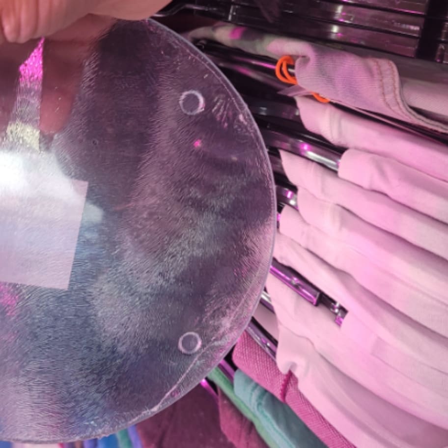 A person holding a round plastic plate in front of a pile of shirts.